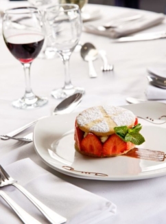 Strawberry dessert on white plate on a white table with a glass of red wine