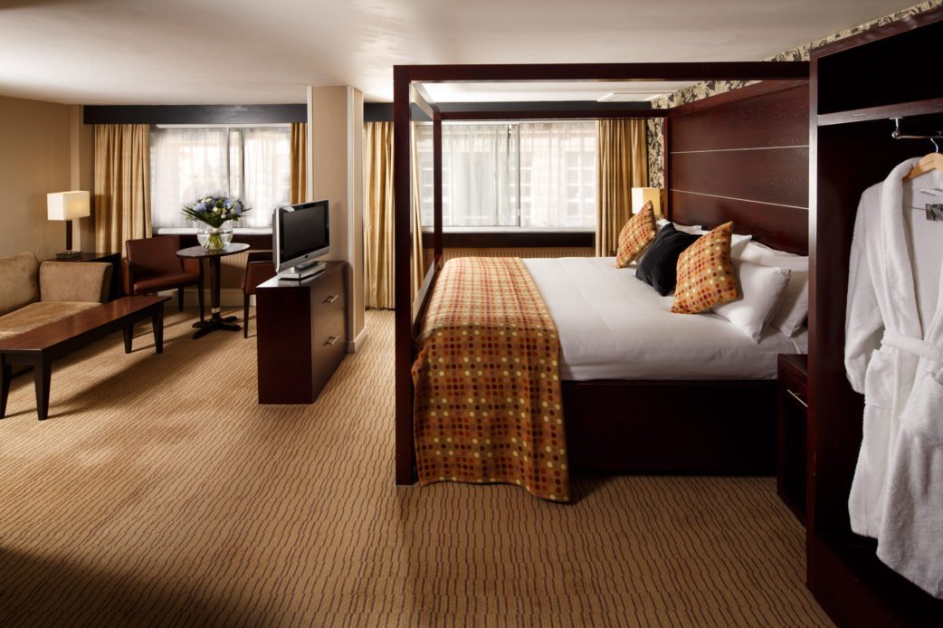 A four poster bed, tv stand and table and chairs in a superior suite at mercure glasgow city hotel