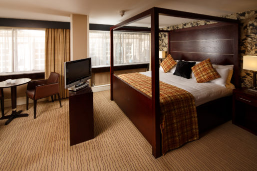 A four poster bed, tv stand and table and chairs in a superior suite at mercure glasgow city hotel