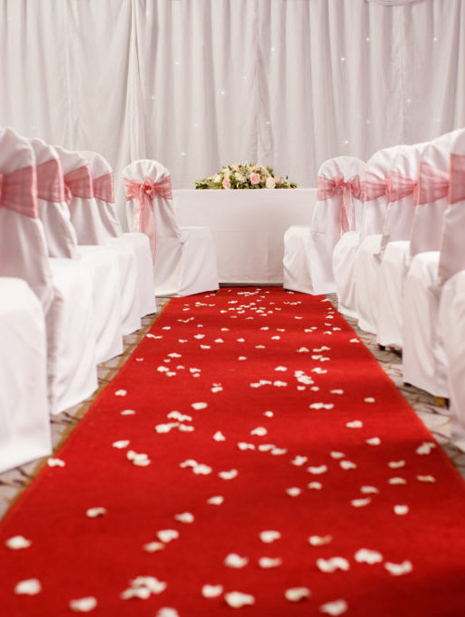 Red carpet with chairs arranged either side dressed with red ribbons, with flower petals scattered over leading to an altar for a civil wedding ceremony at mercure hotels