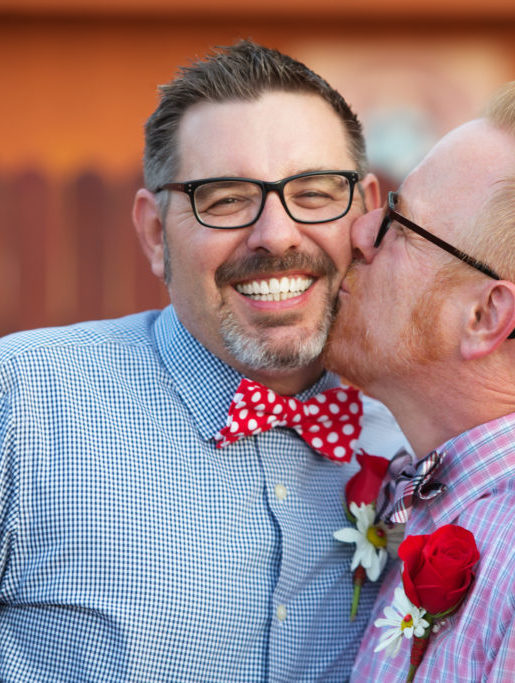 Smiling man with eyeglasses being kissed by spouse