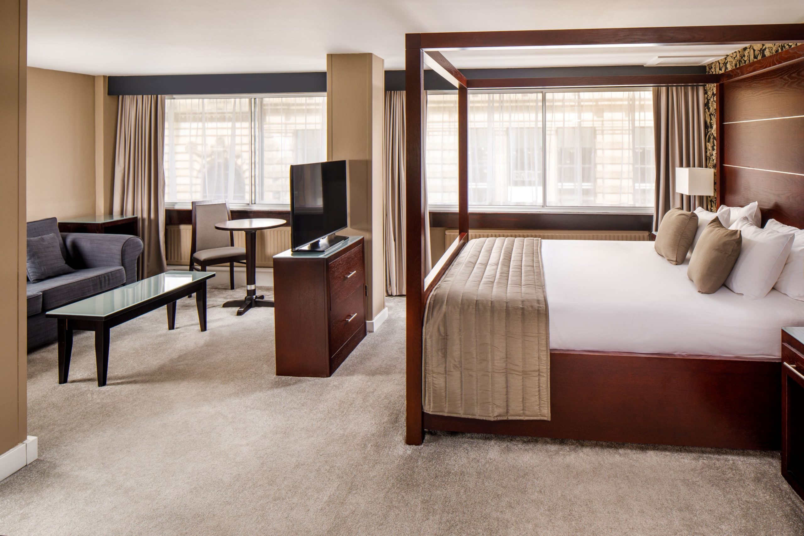 Mercure Glasgow Superior Bedroom A four poster bed, tv stand and table and chairs in a superior suite at mercure glasgow city hotel